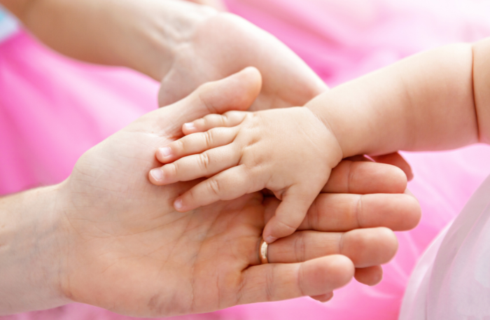 Manina di neonato accolta da due mani adulte, immagine simbolica per comunicare nel materno infantile con delicatezza