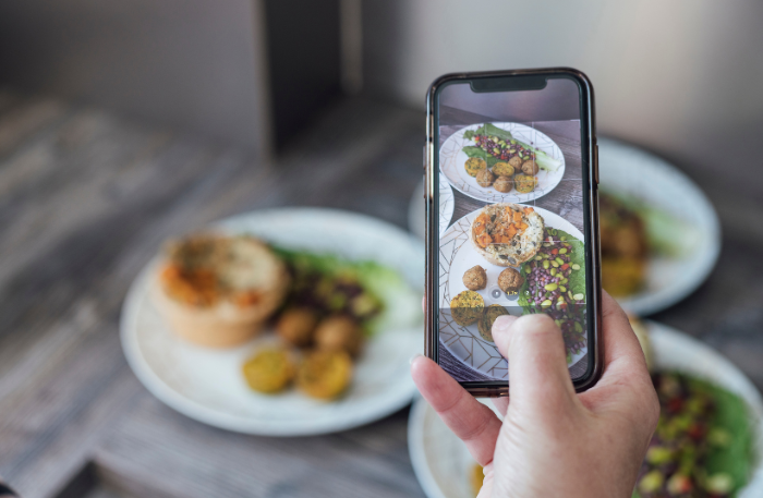 Una mano con uno smartphone che scatta una fotografia a un piatto per spiegare che esiste il cambio di prospettiva